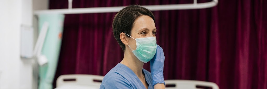 Infirmière masquée en tenue médicale ajustant un gant dans un couloir de clinique