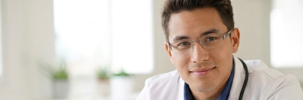 Médecin généraliste souriant en blouse blanche installé à son bureau de consultation